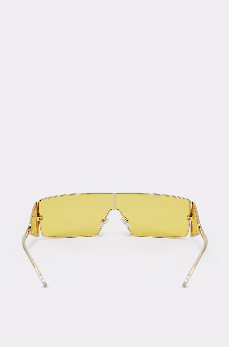 LEMON TWIST SUNGLASSES: Rectangular yellow shield shades with a single yellow-tinted lens, thin gold metal frame, and straight arms—a bold festival accessory, displayed on a plain white background. 3