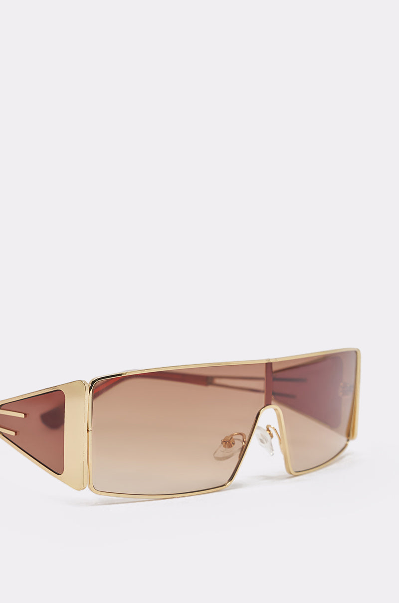 VIXEN SUNGLASSES: Gold-framed oversized retro shield sunglasses with gradient brown lenses, wide arms, and a minimalist modern design, shown on a plain white background. 4