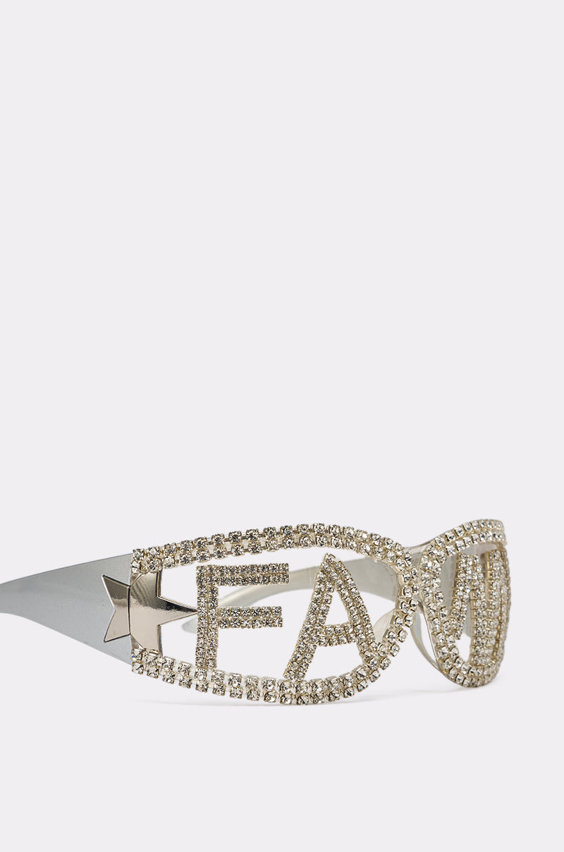 FAME SUNGLASSES: Silver festival shades with oversized frames outlined in rhinestones. "LEAVE" appears in bold capitals across the frames, and a star detail accents the arms near the hinges. White background. 4