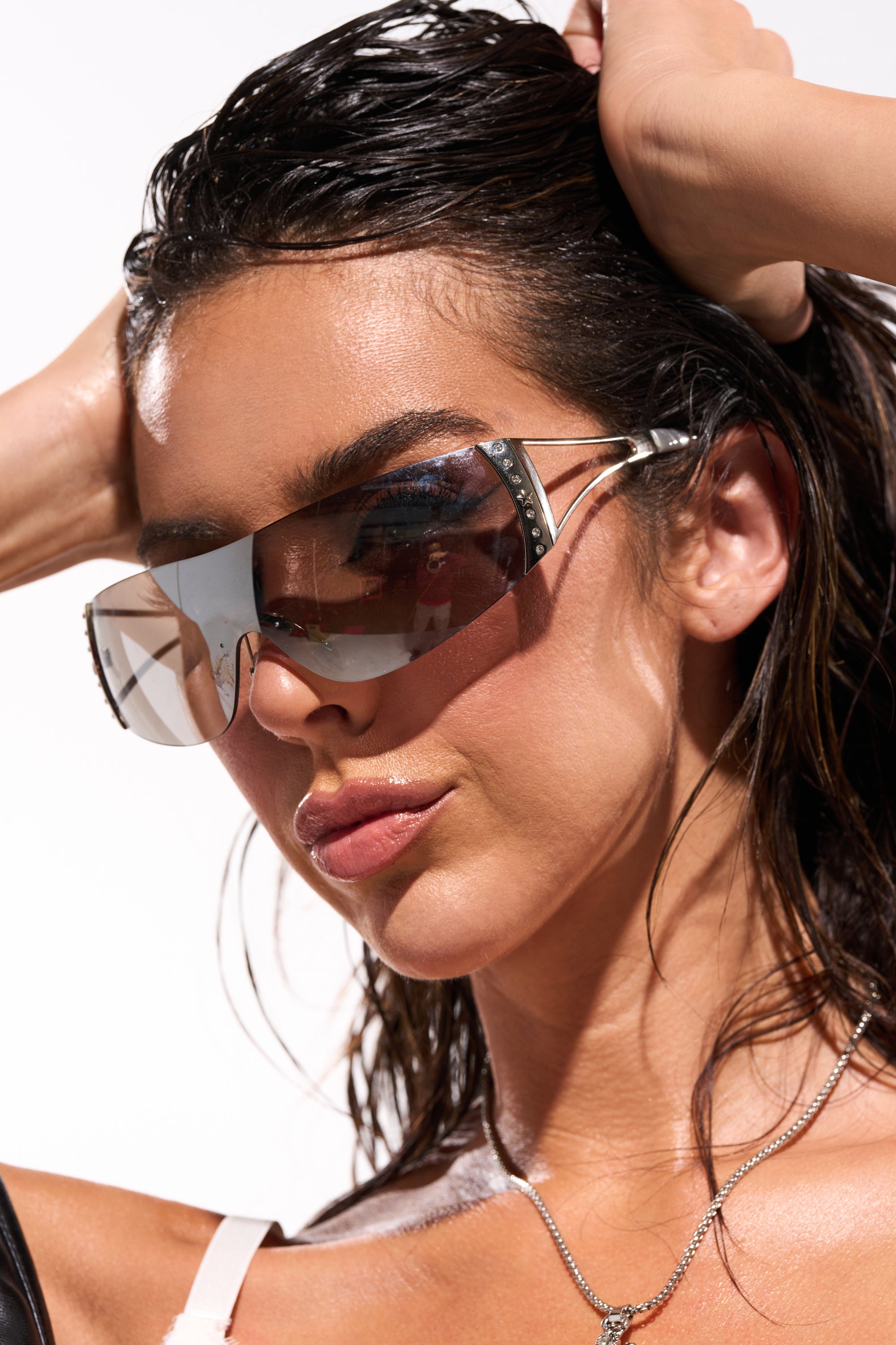 A woman with wet, slicked-back hair and a silver necklace poses in EVERY DAY SUNGLASSES—oversized crystal shield frames—paired with a thin-strapped top against a bright background. 0
