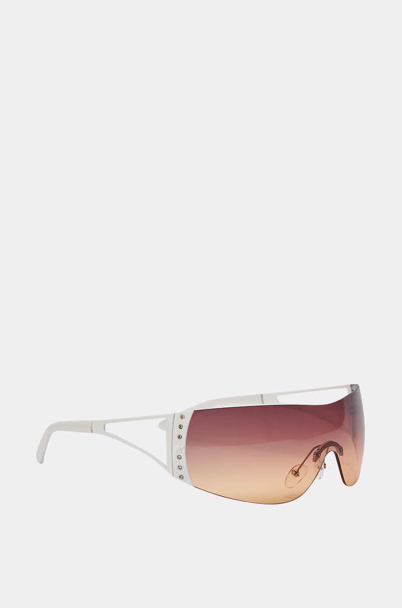 NEUTRALEYES SUNGLASSES feature a Y2K-inspired shield design with a single gradient lens fading from brown to pink, white arms, and small metallic studs along the sides, shown against a plain light background. 2