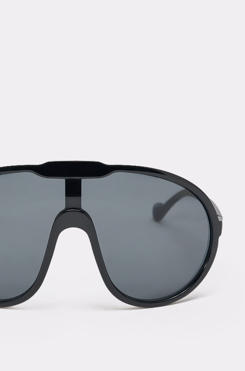 Close-up of BIGGER IS BETTER BLACK SUNGLASSES featuring a single, continuous dark lens and thick black frame against a light gray background. Only the right half of these sporty sunglasses is shown. 4