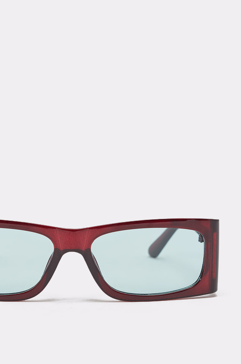 Close-up of KEKE SUNGLASSES featuring a geometric frame with a shiny dark red finish and light blue-tinted lenses, set against a plain white background. 4