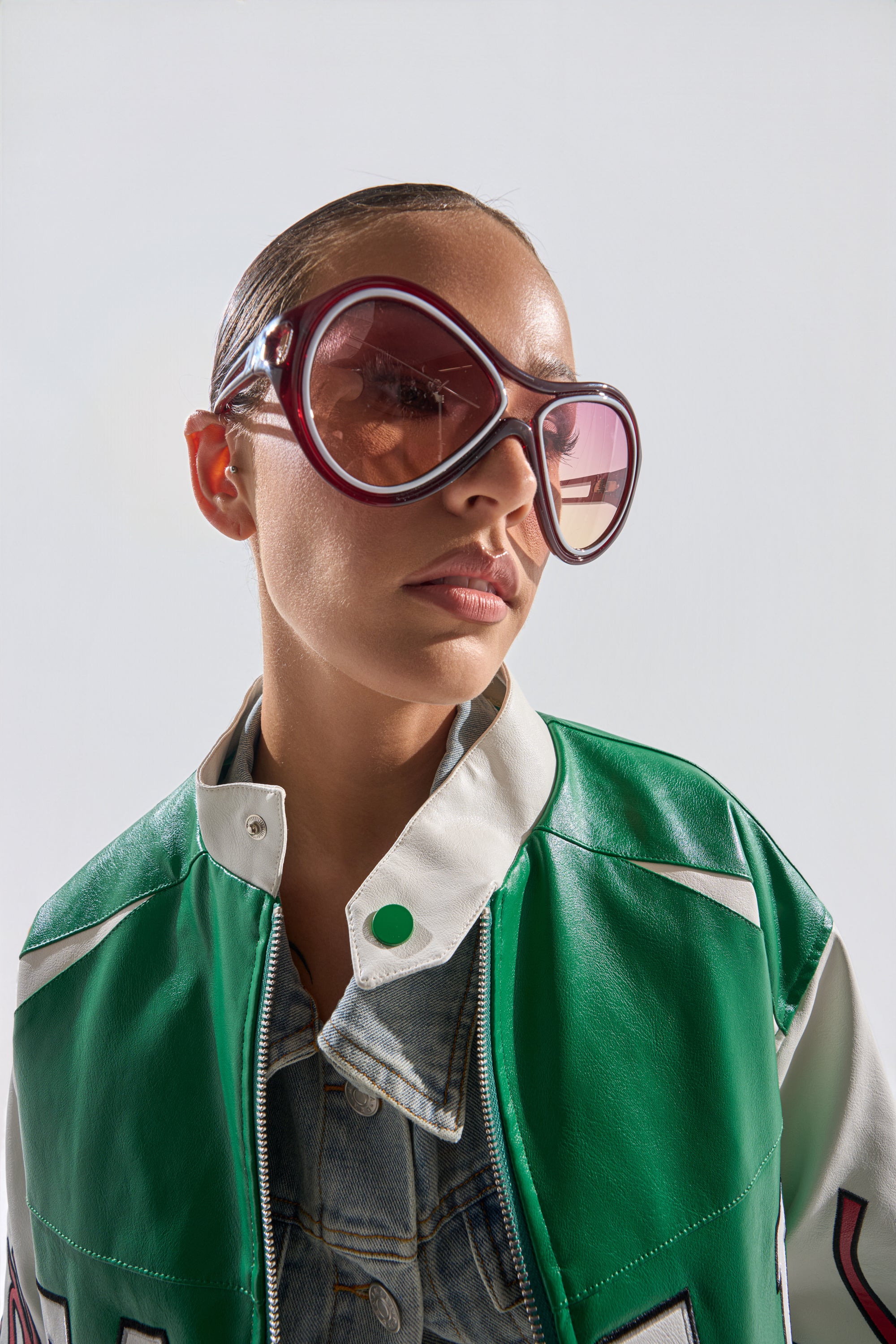 Wearing WILLY SUNGLASSES, a person with slicked-back hair, a green and white leather jacket, and a denim shirt looks confidently to the side against a plain background. 0