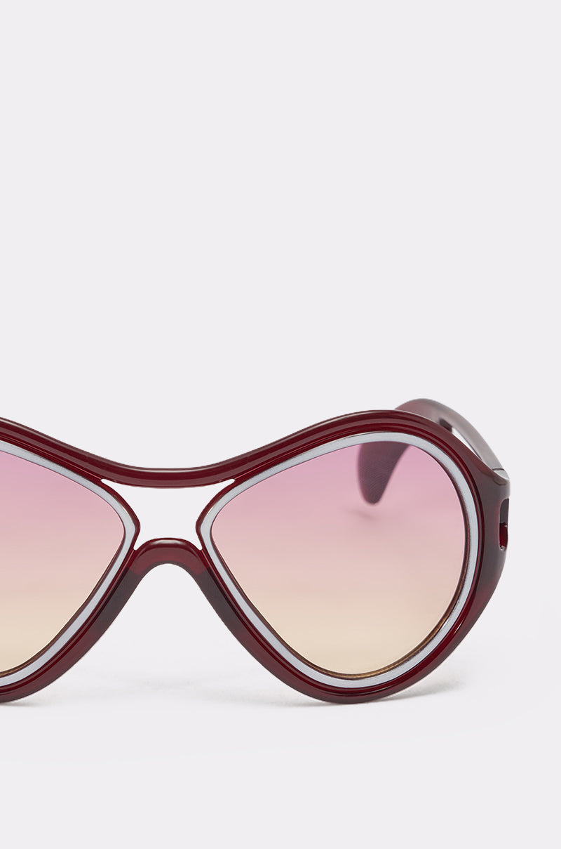 Close-up of WILLY SUNGLASSES featuring large, rounded frames and pink gradient lenses. Only one lens and part of the retro-inspired frame are visible against a plain white background. 4