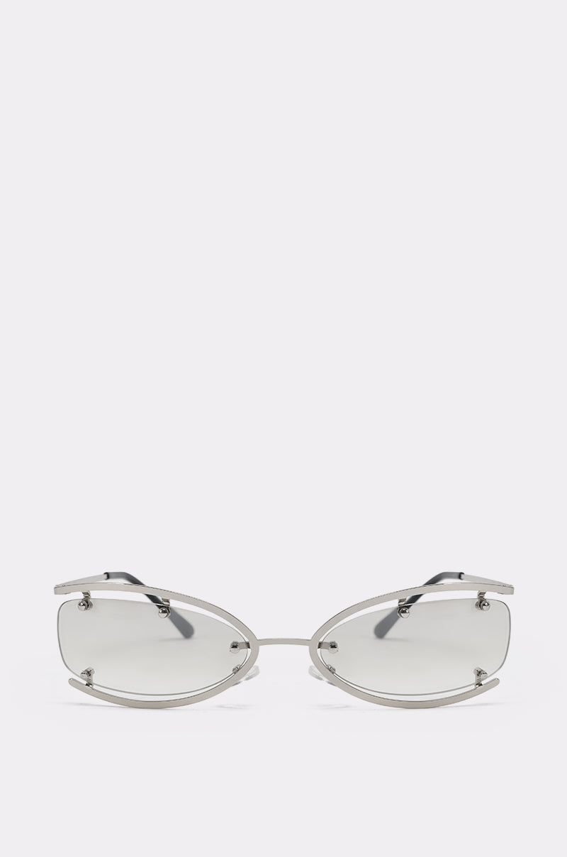 The U SEE ME GLASSES are futuristic oval sunglasses with silver-tone metal frames, lightly tinted lenses, and exposed screws, shown against a plain light background. 1