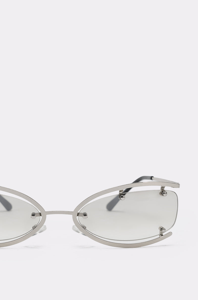 The U SEE ME GLASSES are silver cat-eye sunglasses with a silver-tone metal frame and lightly tinted lenses. Their minimalist oval design and geometric details stand out against a white background, with only the upper half visible. 6