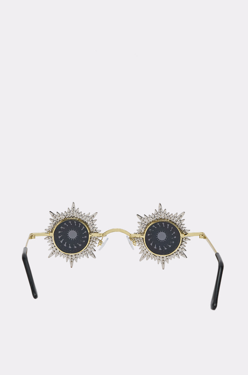 The WHY DO I NEED TO SEE SUNGLASSES feature gold frames, spiked sun-shaped rims, and round black lenses with eye and celestial symbol illustrations. 2