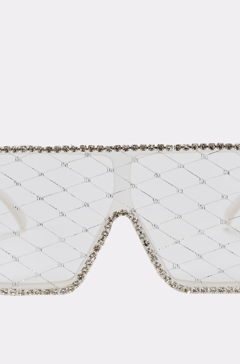 Close-up of BEEZ SUNGLASSES—oversized shield style with a geometric quilted lens pattern and sparkling rhinestone trim accenting the outer edge of the clear frame. 3