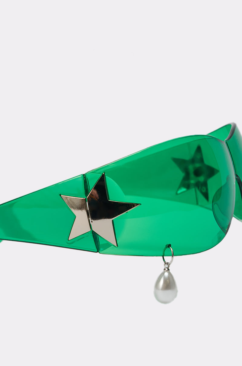 The I DONT CRY SUNGLASSES feature green shield lenses, a metallic gold star accent on the side, and a dangling pearl-like charm. Their bold wraparound design and tinted lenses add a modern, futuristic vibe. 3