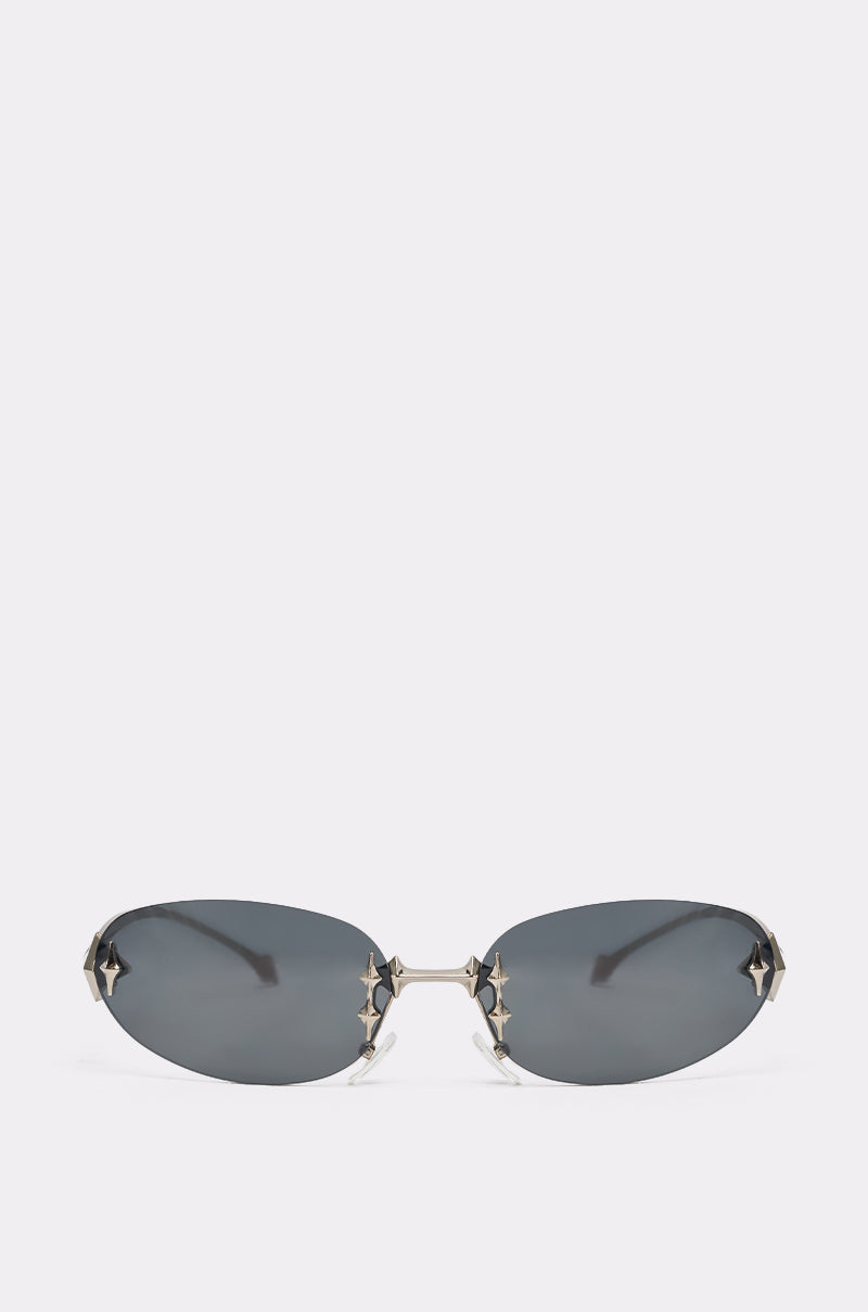 CYBER SUNGLASSES: Y2K oval frames with dark tinted lenses and silver star-shaped accents at the corners and bridge, shown on a plain light background. 1
