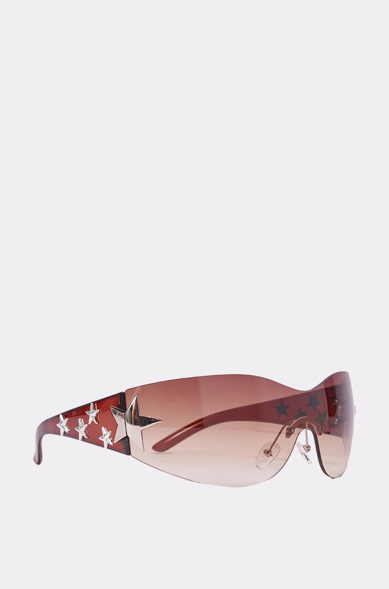 The HOTTIE ALERT SUNGLASSES feature a brown gradient wraparound design with maroon tinted lenses, wide arms embellished with silver stars, and a large silver star accent by the temples against a light background. 0