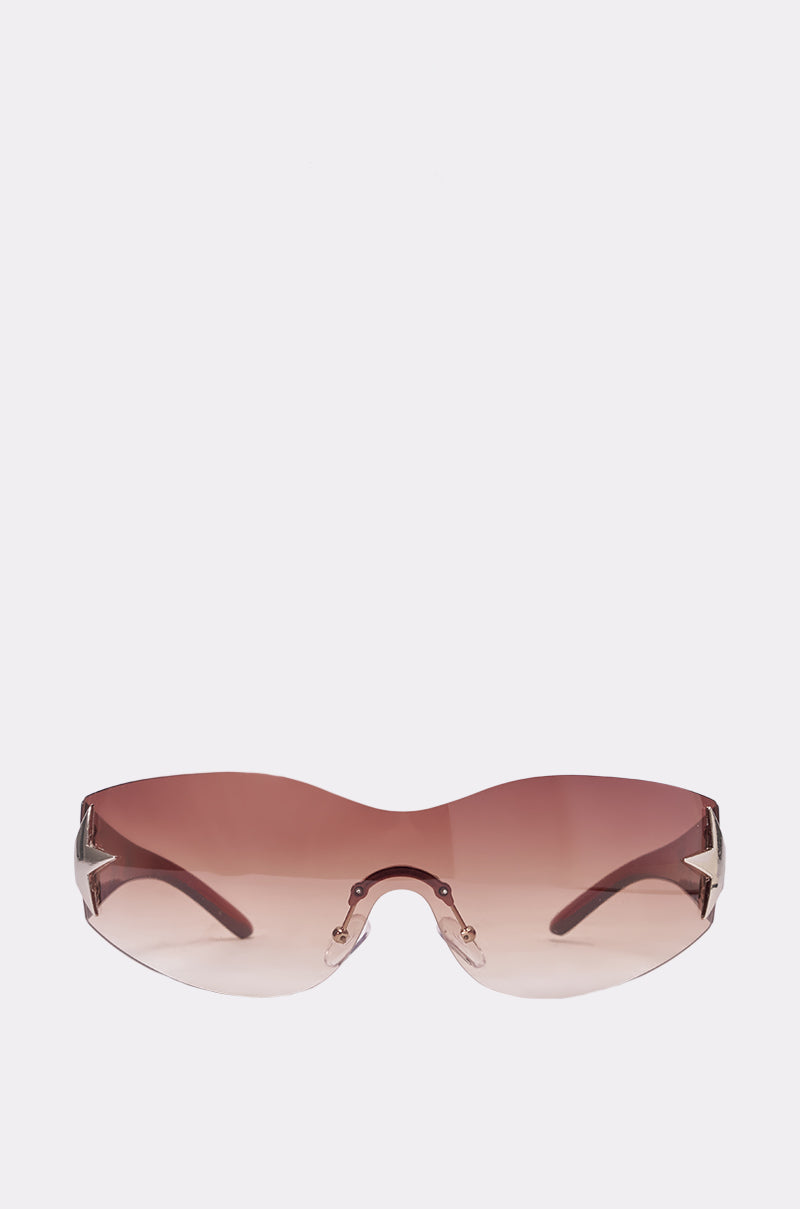 The HOTTIE ALERT SUNGLASSES are oversized, frameless festival shades featuring rose-tinted gradient lenses and thin arms, shown against a plain light background. 3