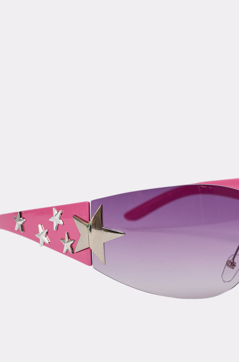 Close-up of MIMI SUNGLASSES: pink shield frames with purple gradient lenses, adorned with silver and gold star studs on the sides—ideal for a trendy festival look. 4