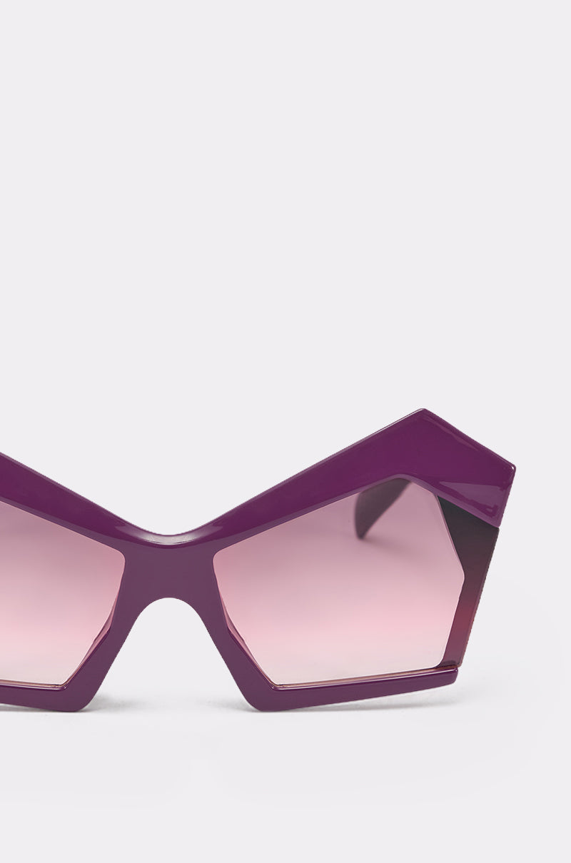 Close-up of ON TREND SUNGLASSES featuring a bold, purple geometric design with a shiny frame and pink-tinted lenses, making these oversized shades stand out against a plain white background. 4