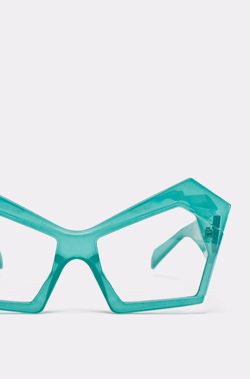 The KYLEIGH GLASSES feature teal, geometric cat-eye frames with thick, angular design and oversized square lenses, shown against a plain light background. 5