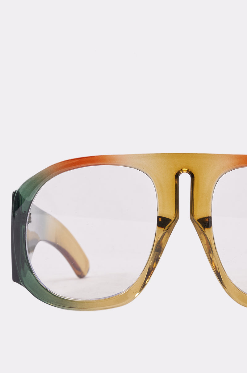 A close-up of IT GIRL GLASSES—stylish, oversized green frames with a marbled gradient pattern (green left, orange top, yellow and brown bottom) and clear lenses—set against a crisp white background. 4