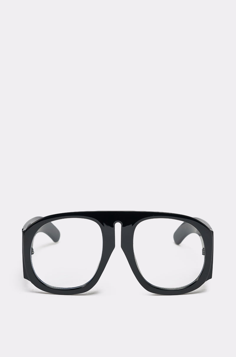 The READ ME GLASSES feature a bold black frame with an oversized, thick design and clear lenses, shown on a plain light gray background. 0