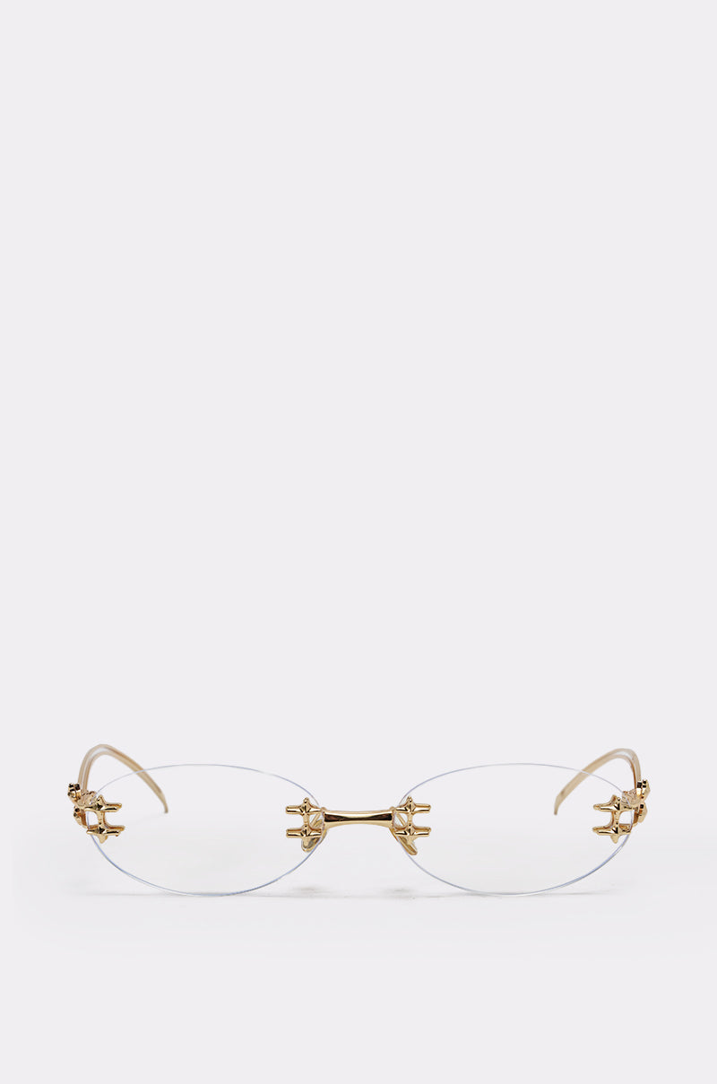 The TREND DRIVEN GLASSES feature a rimless oval design with a gold-tone metal frame and ornate, claw-like gold accents at the hinges, showcased against a plain light background. 1