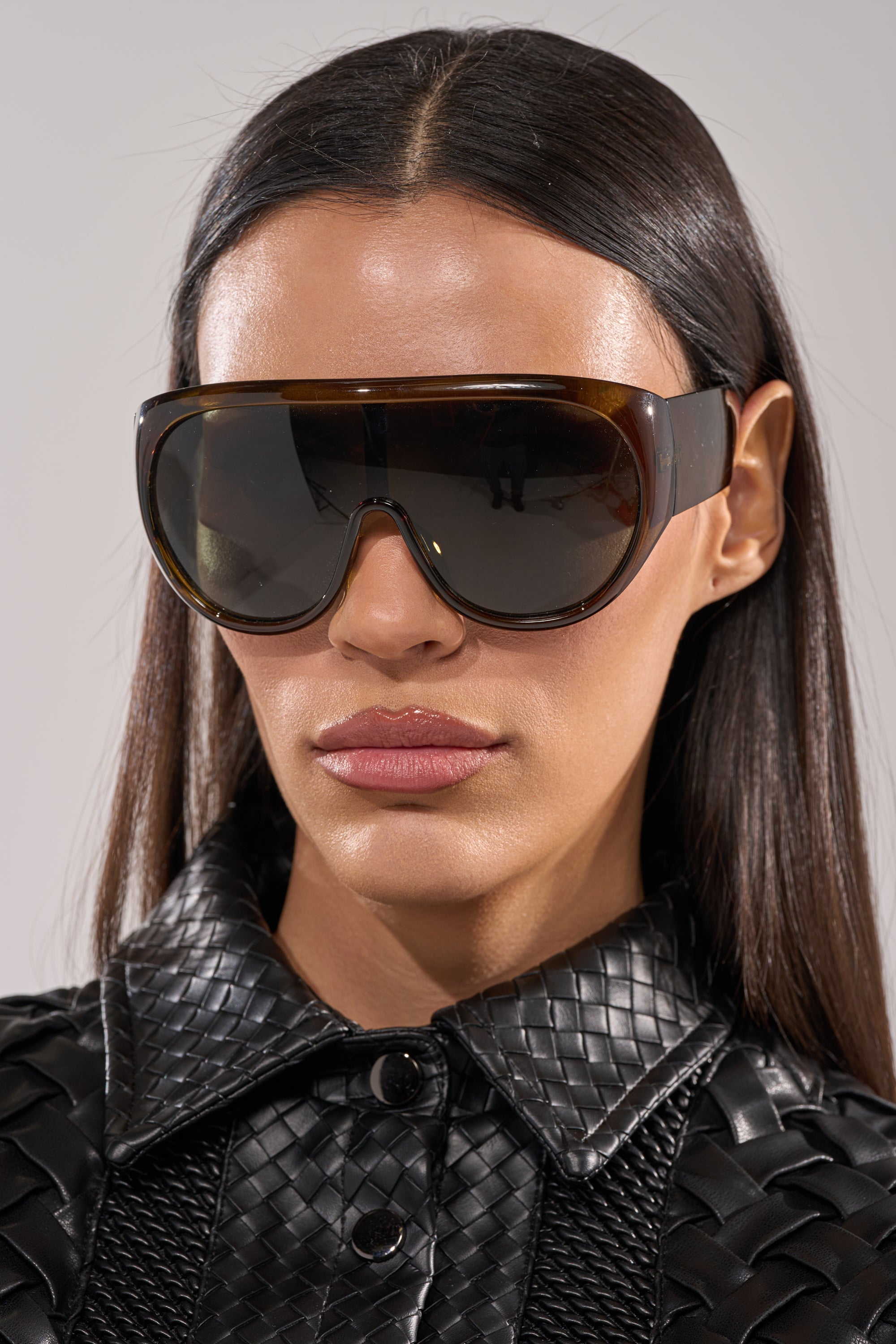 A woman with straight dark hair wears TOMBOY SUNGLASSES and a black textured leather jacket, looking forward with a neutral expression. 3