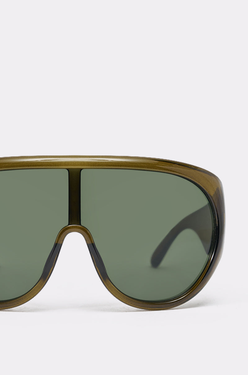 Close-up of TOMBOY SUNGLASSES in olive green, showcasing an oversized shield style with a wide single lens and thick frame—bold streetwear sunglasses—photographed against a plain light background. 5