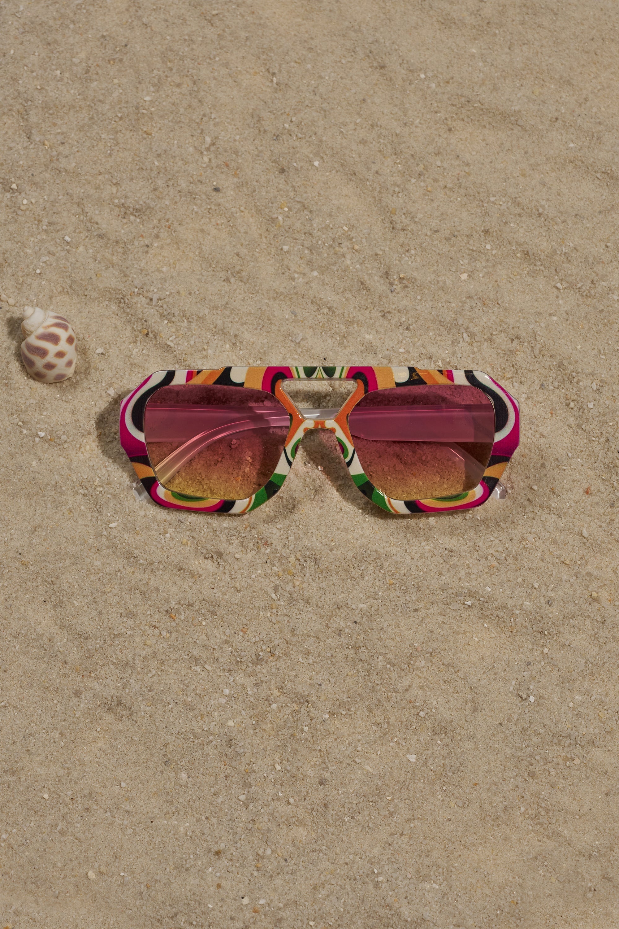 FEEL THE BEAT SUNGLASSES with multicolor square frames and pink lenses rest on sand beside a spiral seashell, perfect for festival vibes. 0