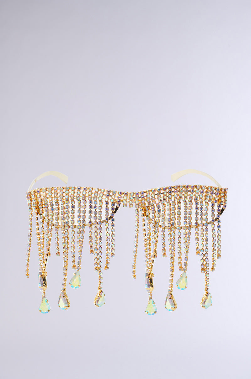 The I DONT CRY SUNGLASSES features a lavish design with a gleaming gold metal frame adorned with rhinestones, dangling crystal-like teardrops, and a rhinestone fringe, creating an opulent and ornamental allure.