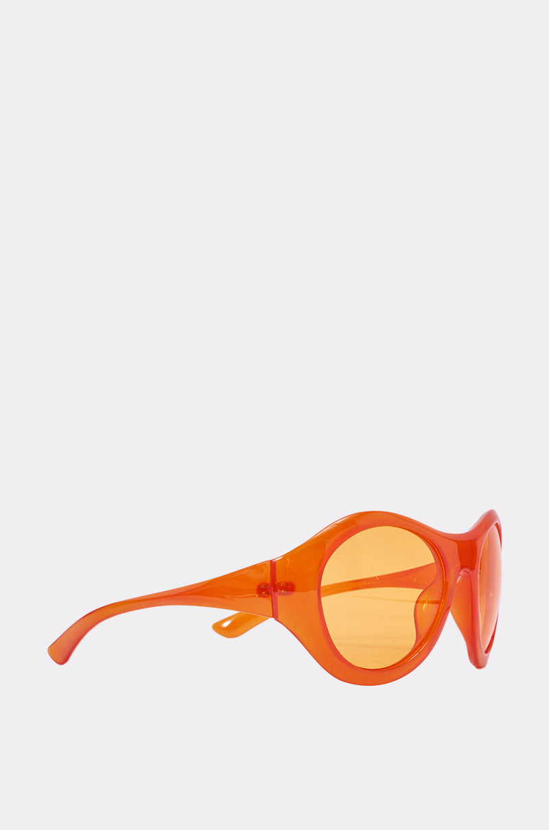 The IN YOUR WORLD SUNGLASSES feature bright orange, oversized round frames and matching orange-tinted lenses, shown from the side on a plain light gray background—ideal for bold summer style. 3