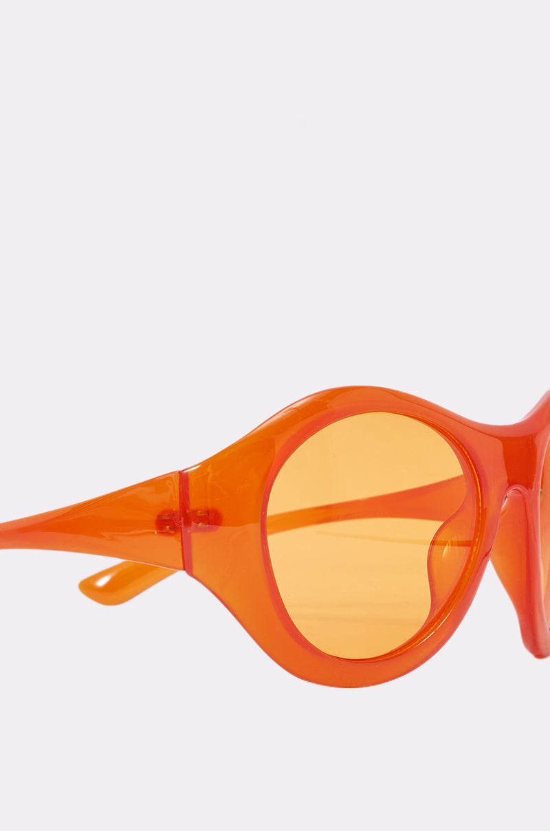 Close-up side view of IN YOUR WORLD SUNGLASSES: bright orange, oversized retro frames with orange-tinted lenses set against a plain light background. 4