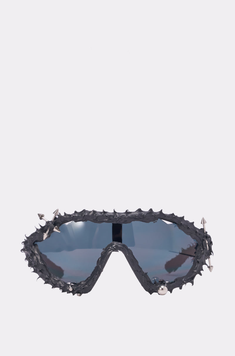 The DANGER SPIKES SUNGLASSES feature a rough black frame, bold silver spikes around the edges, and reflective blue lenses for a fierce statement. Shown against a plain light gray background. 0