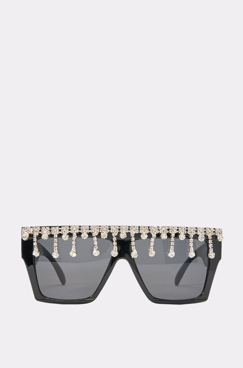 The DIAMOND SHIELD SUNGLASSES are glamorous black shield sunglasses with dark lenses, adorned with a row of sparkling rhinestones and dangling crystal strands along the top edge.