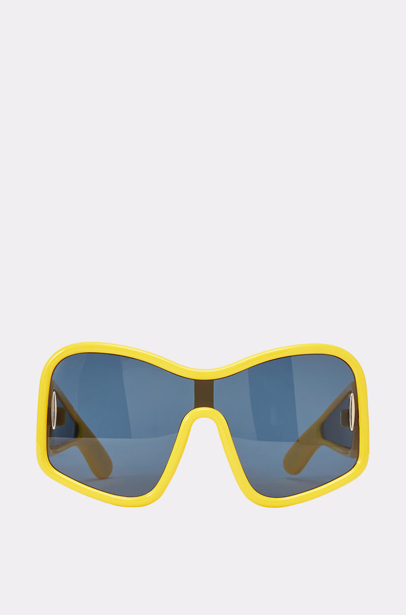 The MAIN CHARACTER SUNGLASSES, featuring yellow rims and oversized shield frames with blue-tinted lenses, are displayed against a plain white background. These sporty sunglasses have arms that are partially visible through the lenses.