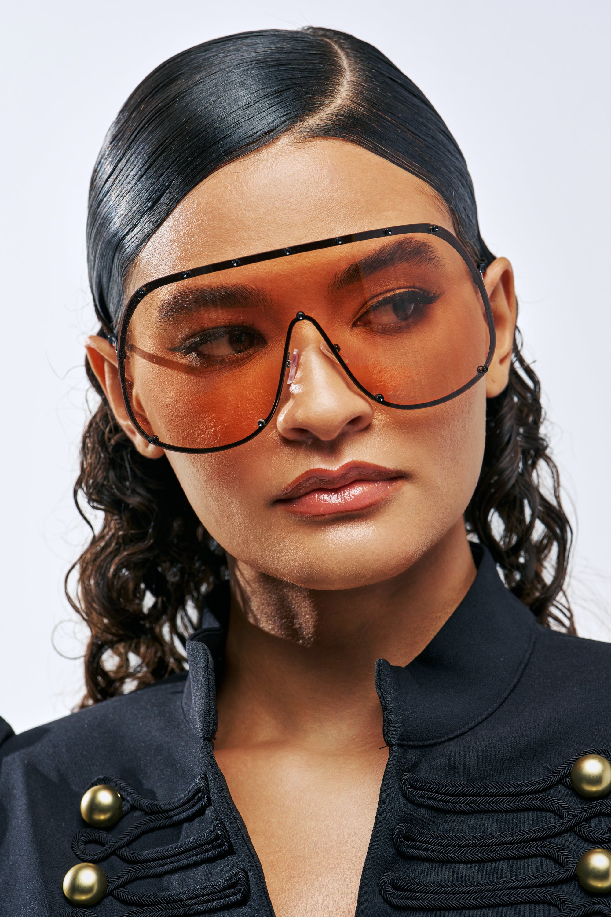 A person wearing TOO FAMOUS SUNGLASSES, which feature large, frameless amber-tinted shield lenses in a streetwear style.