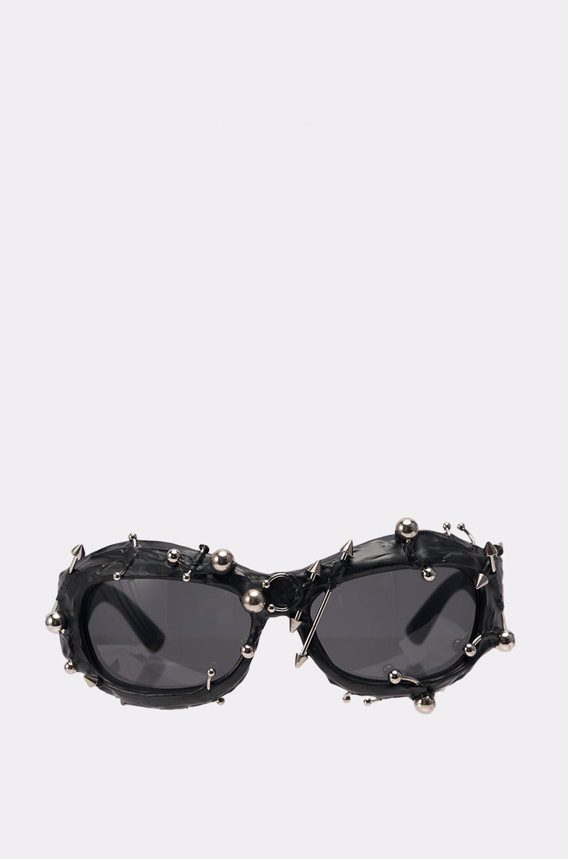 PIERCED VIBES SUNGLASSES feature black oval frames, dark lenses, and metallic studs and spheres for a bold, punk-rock style. Displayed against a plain light background. 0