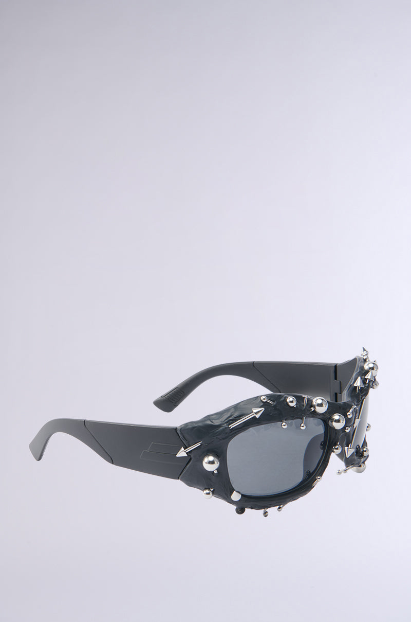 A pair of chunky black PIERCED VIBES SUNGLASSES with dark lenses, featuring silver-tone metallic detailing and decorative accents, displayed on a plain light gray background. 5