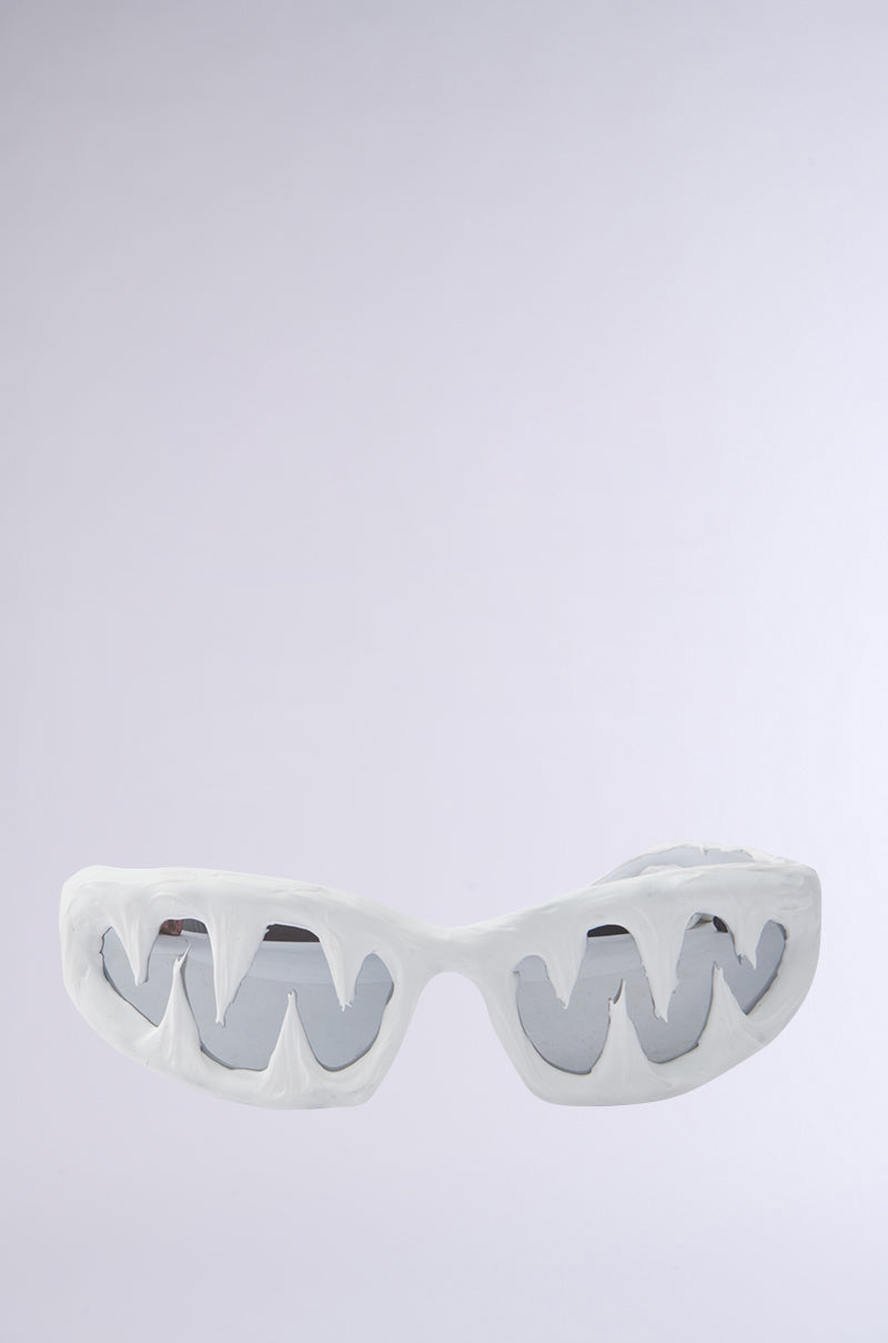 ICED OUT SUNGLASSES with white frames shaped like sharp teeth and icicle-inspired fangs, creating an open mouth look, set against a plain light gray background.