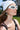 A woman poses outdoors in ICED OUT SUNGLASSES featuring a wavy black pattern, a white beanie, metallic hand-shaped earrings, and a black strappy top with buildings and greenery behind her.