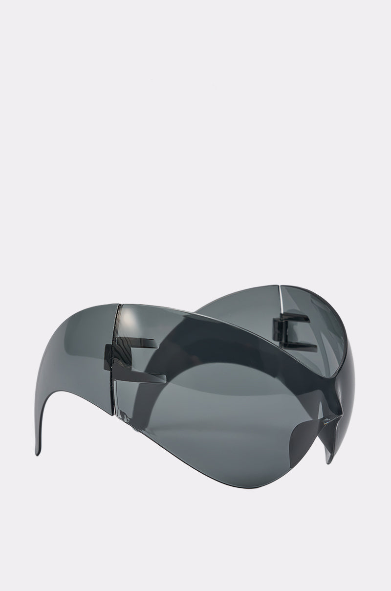 IM BETTER SUNGLASSES: Bold, oversized shield sunglasses with a streetwear-inspired wraparound design and dark grey lenses, frameless for a sleek look. Shown on a plain white background. 3
