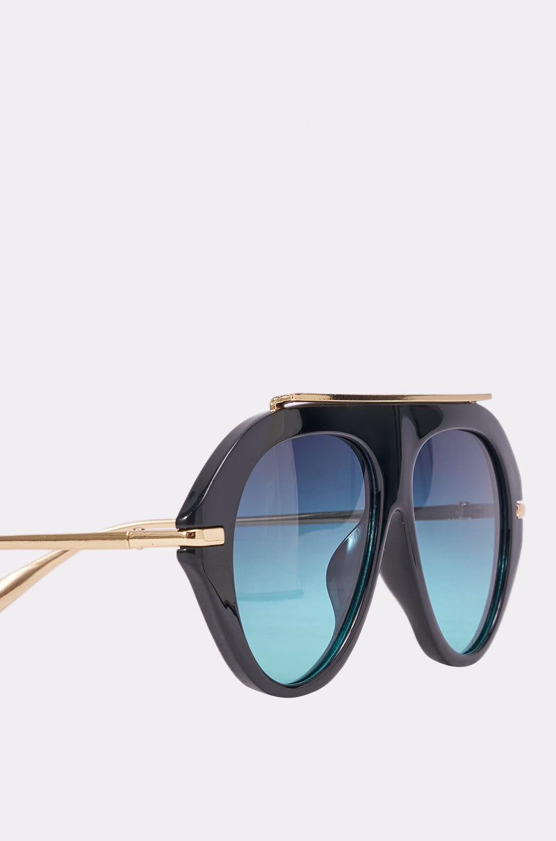 The LUXE AIR SUNGLASSES IN BLACK BLUE feature oversized aviator style with thick black frames, gold metal arms, and blue gradient lenses—angled to showcase their bold shape and metallic accents, perfect for standout summer style. 4