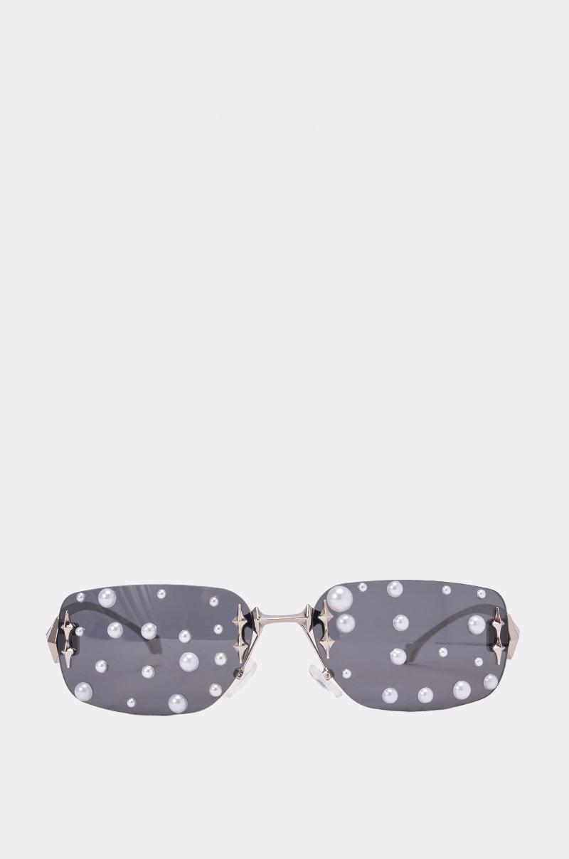 The MIDNIGHT DRIP SUNGLASSES feature rectangular frameless gray lenses, white pearl embellishments, and star-shaped gold details on the temples—perfect statement shades for any festival look. 0