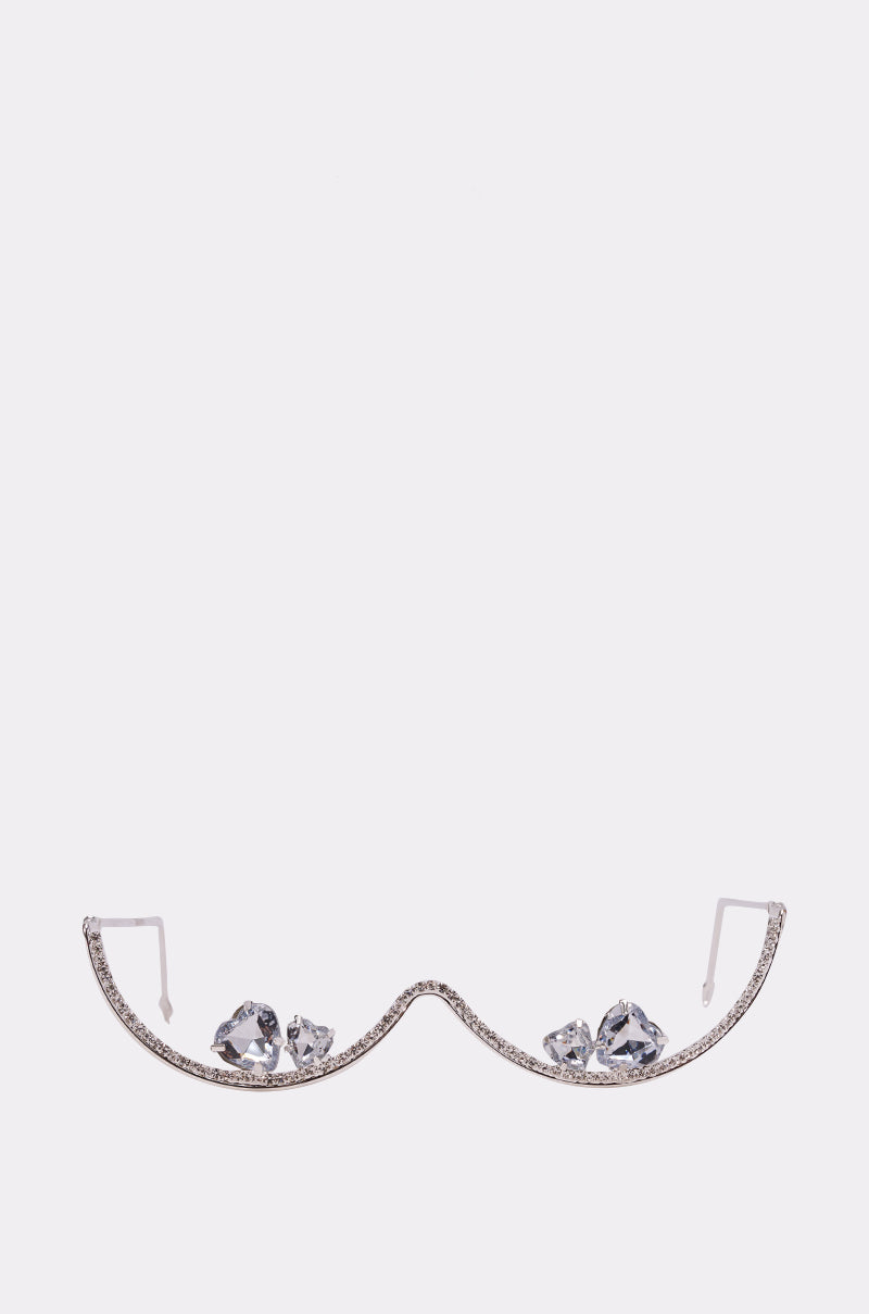 The DIAMOND DRIFT SUNGLASSES feature a curved, minimalist design without lenses and are embellished with large, clear gemstones on each side, displayed on a plain white background. 2