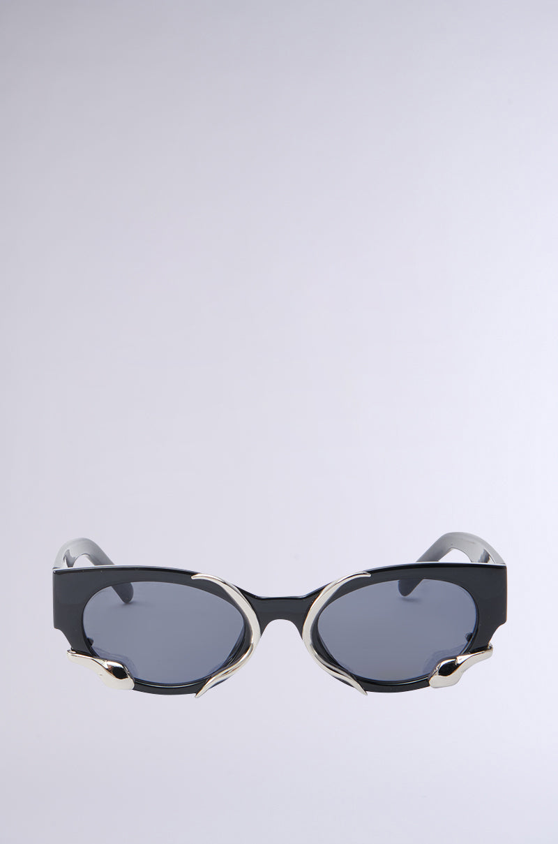Introducing VENOM LOVE SUNGLASSES: fashion-forward black cat-eye frames with metallic snake-inspired side detailing. Featuring dark oval lenses, these bold sunglasses stand out effortlessly against a light gray background.