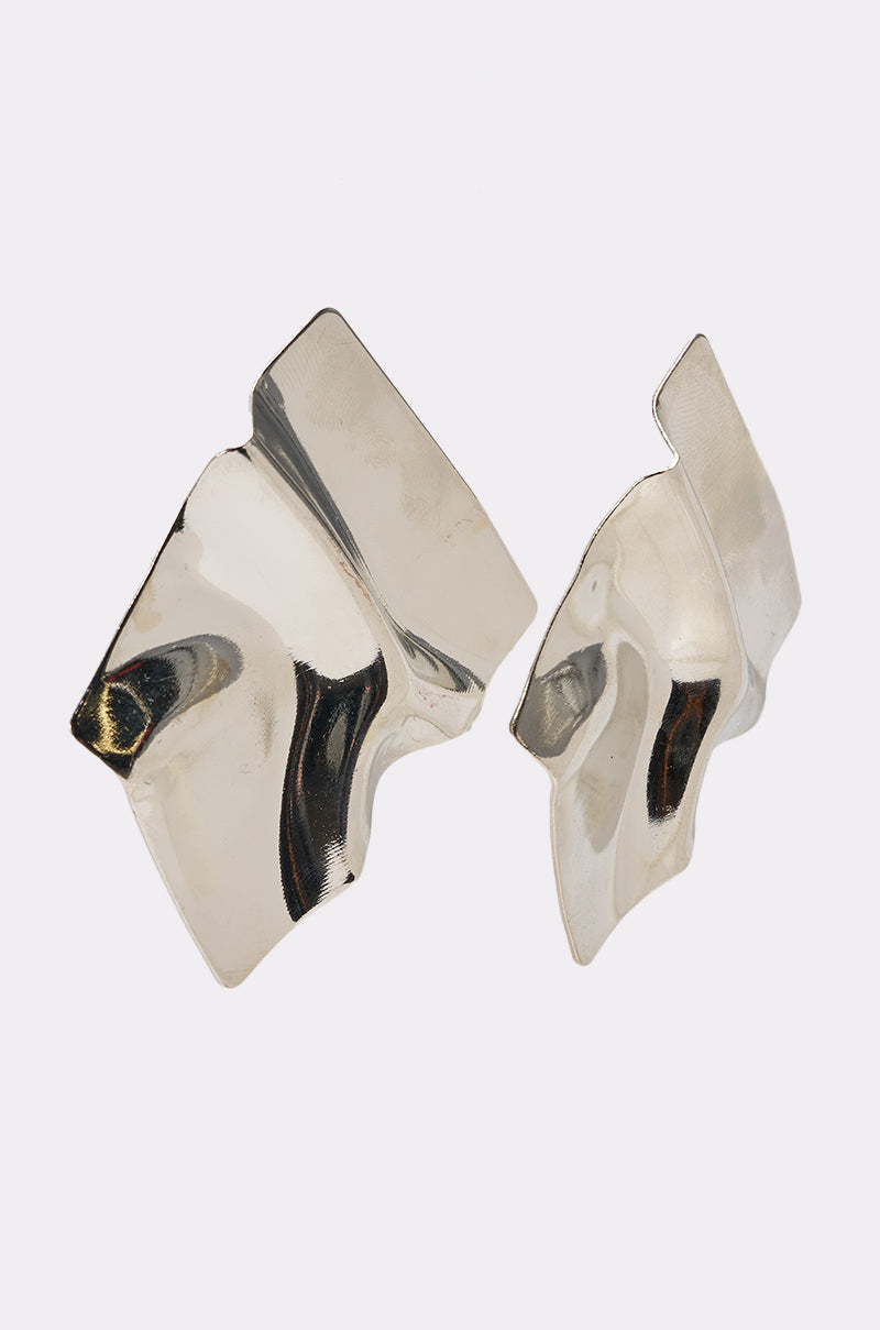 The MIRROR MIRROR OVERSIZED STUDS are abstract, asymmetrical earrings with smooth, wavy reflective surfaces and irregular shapes, displayed against a plain white background. 2