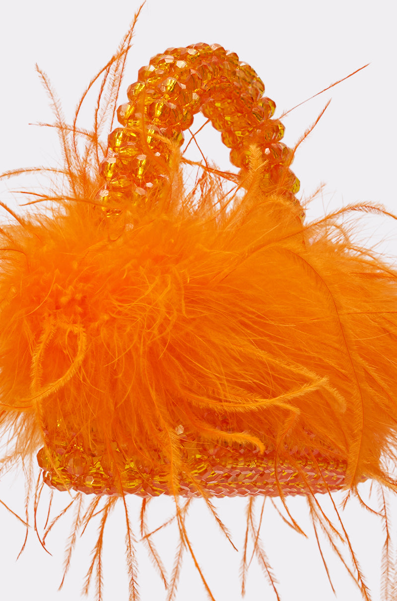 The NIGHT OUT BEADED FEATHER BAG is a small orange handbag with a beaded handle and bold feather trim, featuring bright orange feathers for a playful, textured look. Shown on a plain, light-colored background. 3