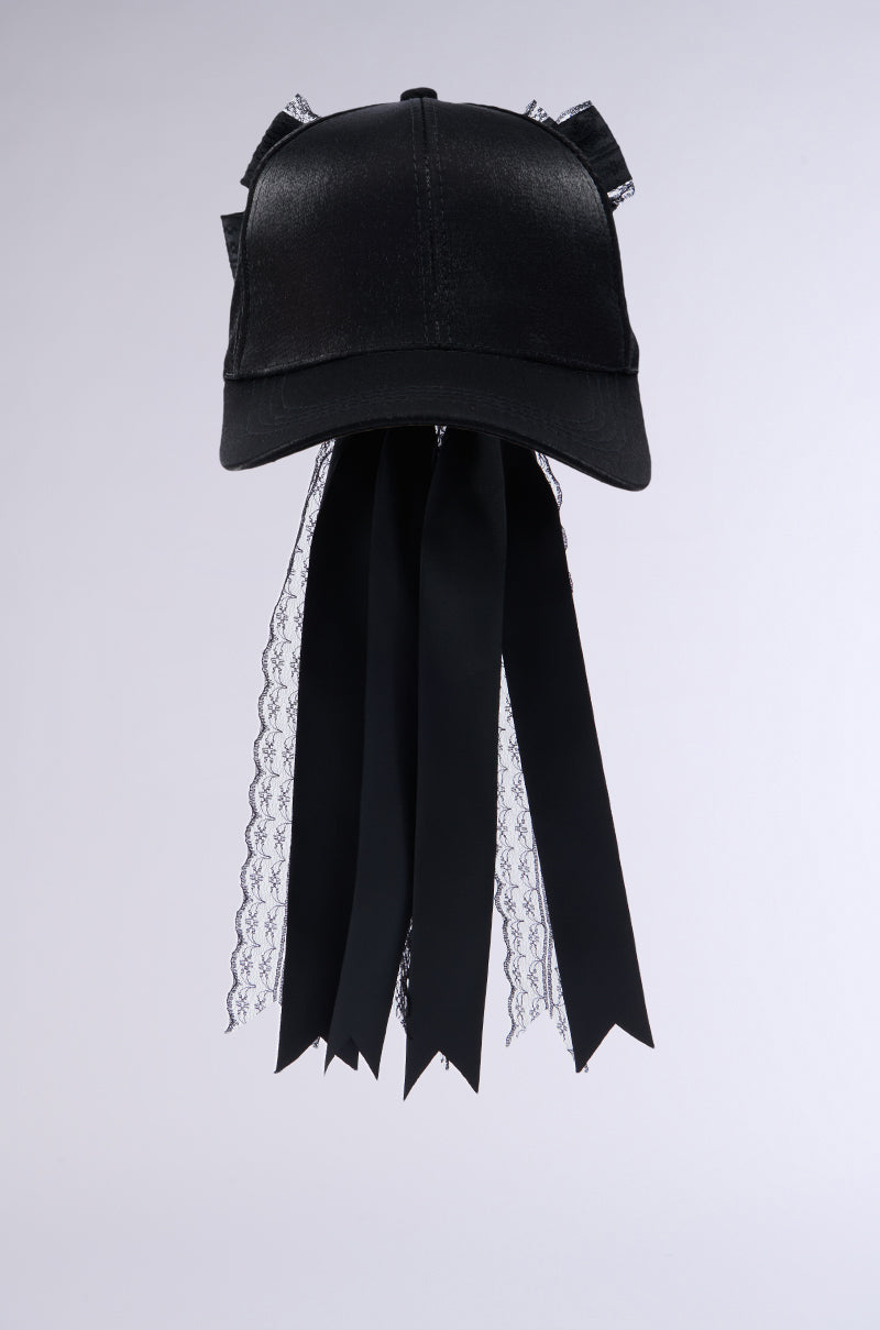 Introducing the ROSA LACE BOW SNAPBACK: a black cap with a shiny finish, adorned with delicate lace accents on the sides and a refined lace bow applique at the back. Long black ribbons cascade down, imbuing the cap with a distinctive gothic flair. Set against a plain white background. 2