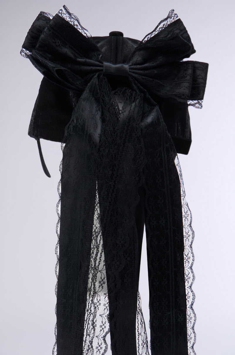 This image showcases the ROSA LACE BOW SNAPBACK, an intricate black lace obi adorned with a prominent lace bow applique and cascading lace details. The elaborate fabric and careful craftsmanship are accentuated against a plain, neutral background. 6