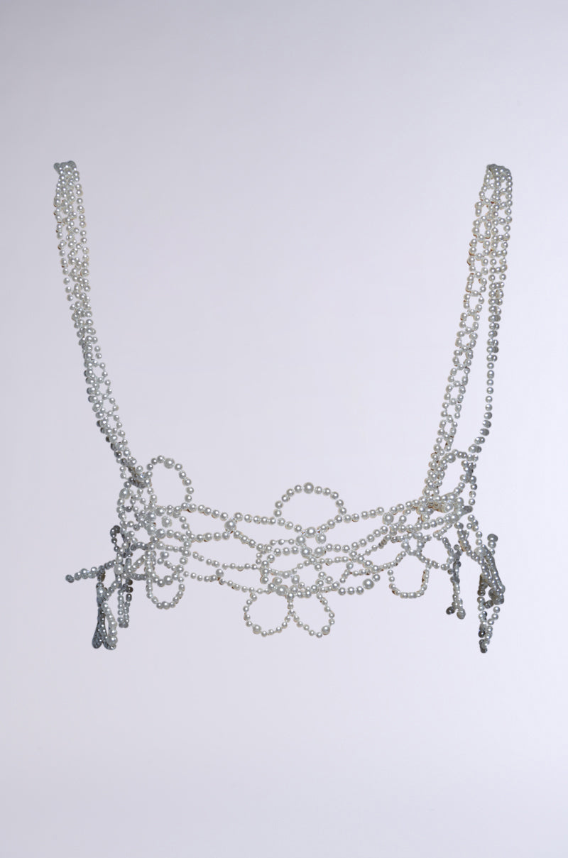The FLOWER BABE PEARL BODY CHAIN is a masterpiece crafted from silver chains and small pearls, featuring floral pearl embellishments and ornate dangling strands. Its delicate design creates an elegant and artistic appearance against a plain, light background.