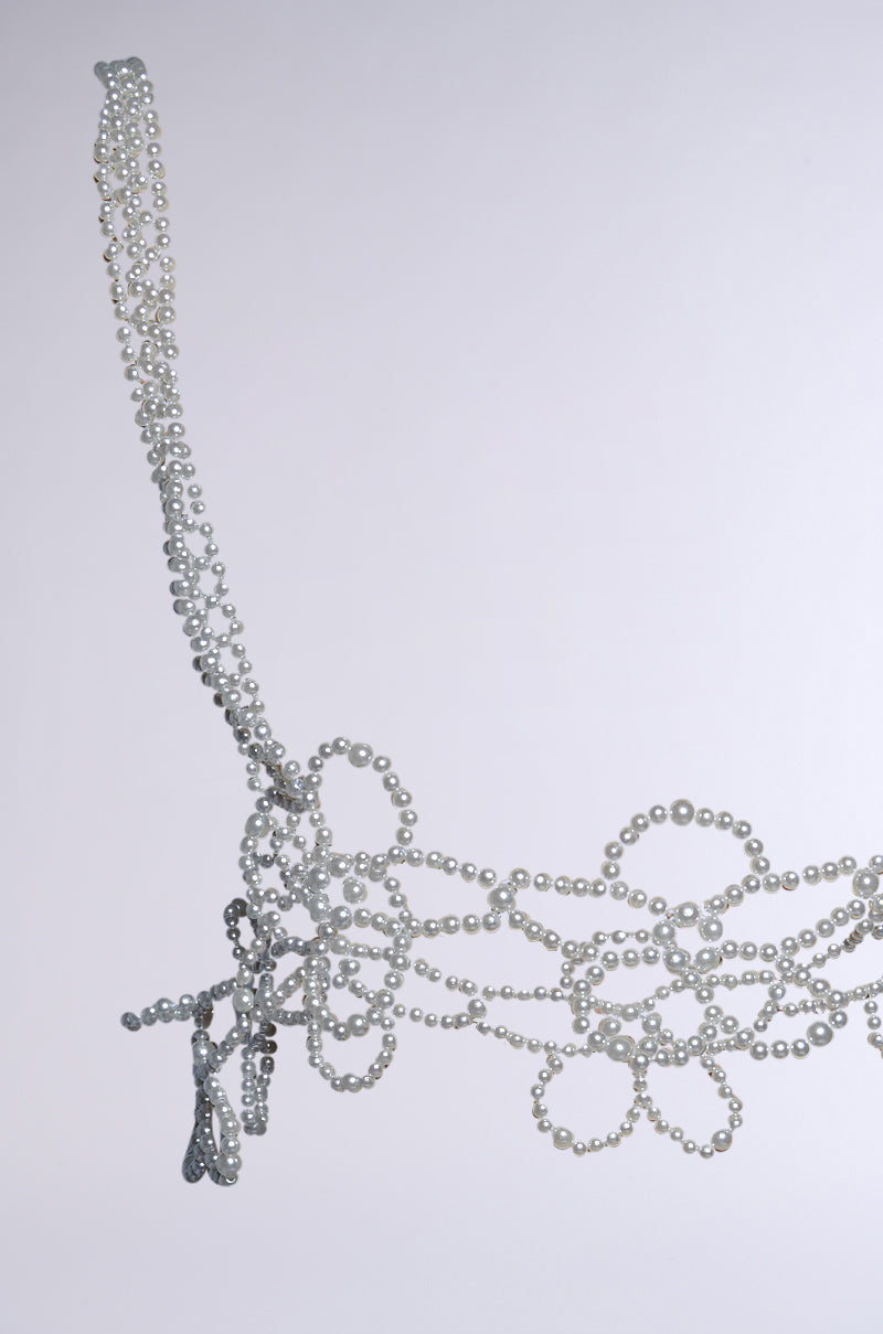 A white pearl and silver metallic bra with floral pearl embellishments and intricate patterns features tank straps and tassels. Photographed against a light gray background, its elegant design pairs perfectly with the FLOWER BABE PEARL BODY CHAIN.