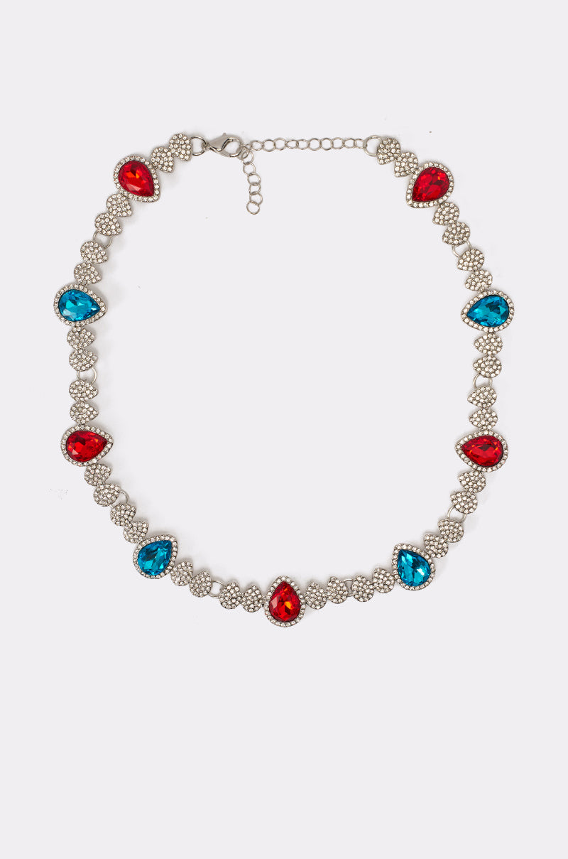 The TOO TURNT RED AND BLUE NECKLACE features alternating red and blue teardrop gems, each framed by clear stones, on a decorative adjustable chain—an eye-catching statement accessory.