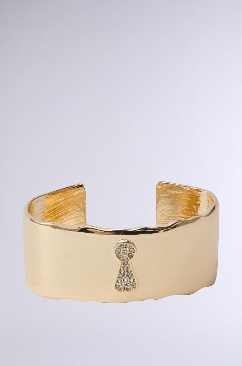 Introducing the "Key to My Heart Cuff," a chunky statement bracelet with a wide band and rhinestone-adorned keyhole design. Its polished finish beautifully catches the light against a neutral backdrop.